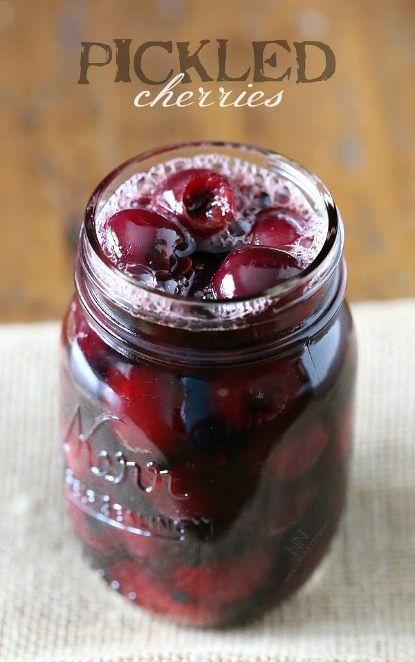 two jars filled with red liquid sitting on top of a wooden table next to a person's hand