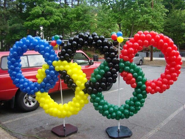 an olympic symbol made out of balloons in a parking lot next to a red car