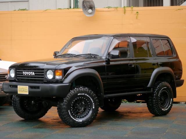 a black suv is parked in front of a yellow wall and another car behind it