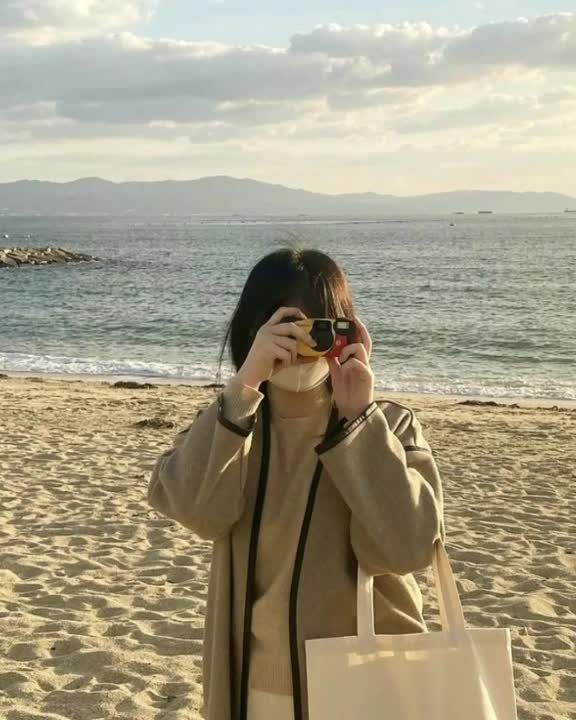 a woman standing on top of a sandy beach holding a camera