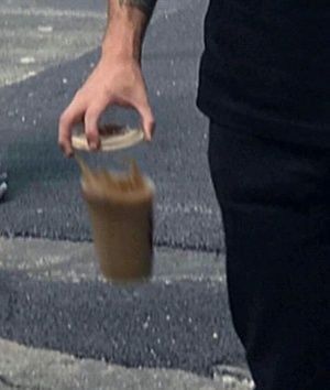 a man is holding a plastic cup with something in it while walking down the street