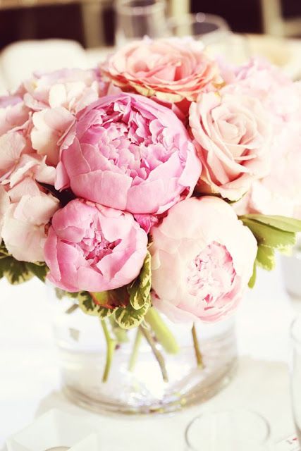 a vase filled with pink flowers sitting on top of a white tablecloth covered table