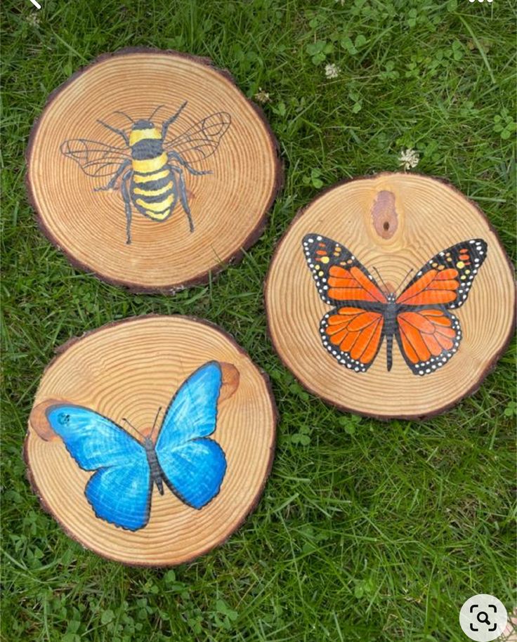 three wooden slices with painted butterflies on them sitting in the grass next to each other