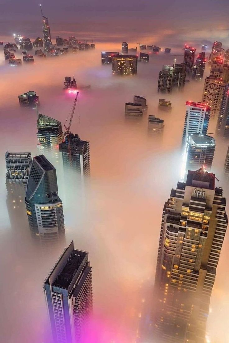 an aerial view of skyscrapers in the foggy cityscape with lights on