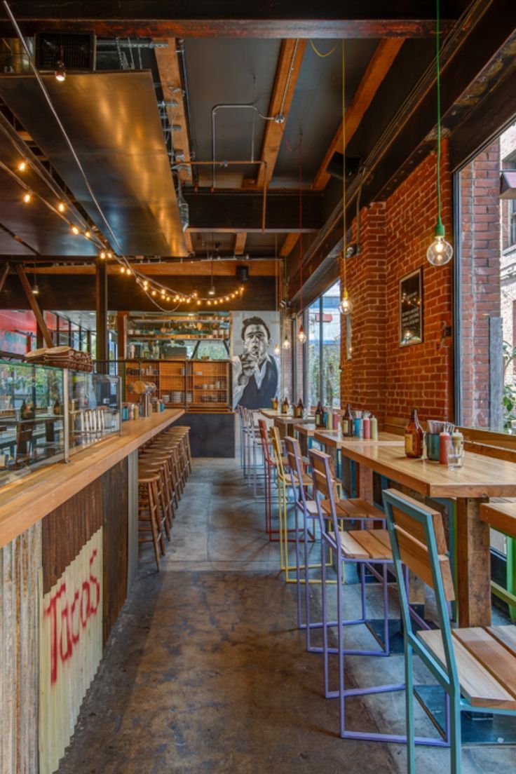 the inside of a restaurant with wooden tables and colorful chairs on either side of the bar