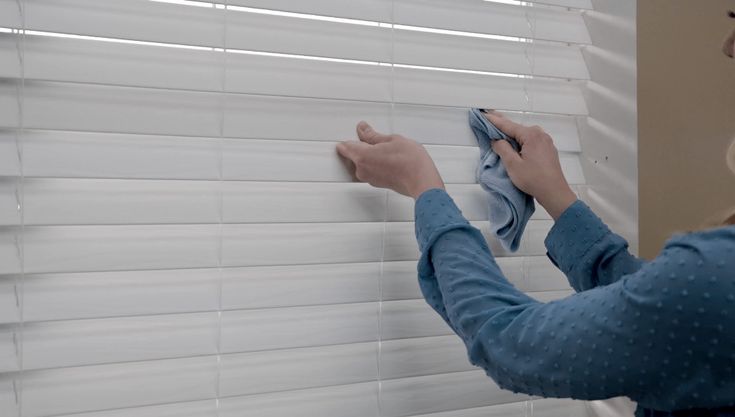 a woman is cleaning the blinds with a cloth