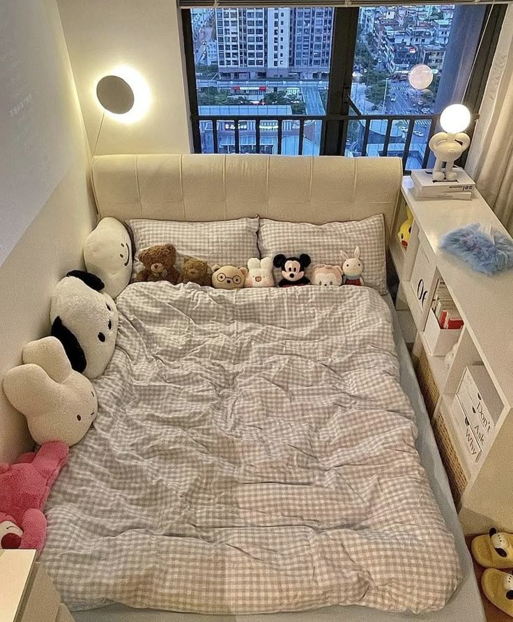 a bed with stuffed animals on it in a room next to a window overlooking a city