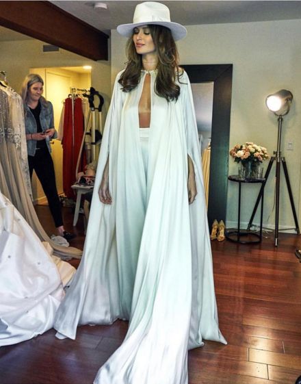 a woman in a white dress and hat standing next to a mannequin on a wooden floor