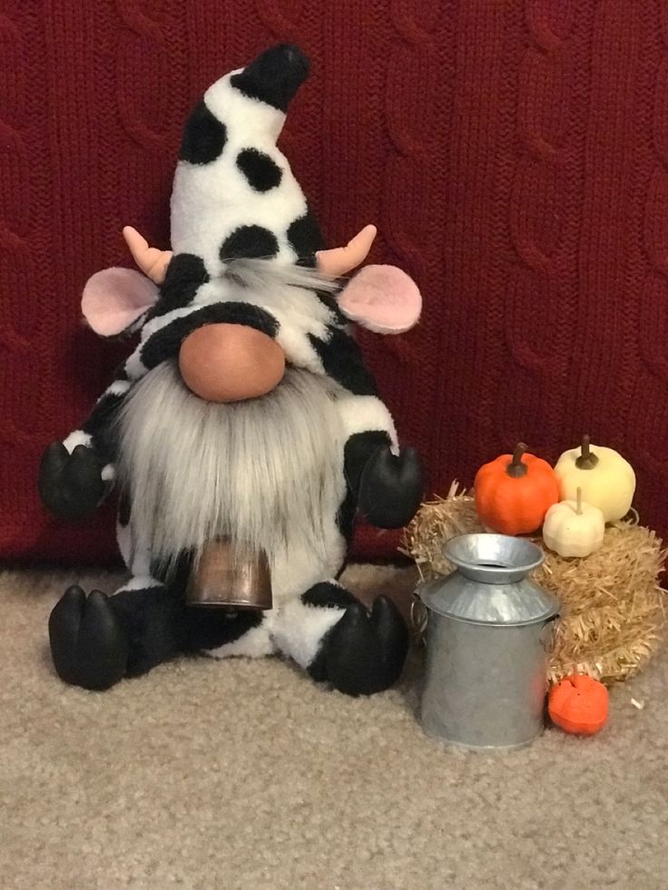 a stuffed cow sitting next to a tin can and pumpkins on the floor in front of a red wall