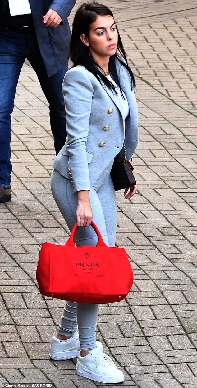 a woman is carrying a red bag while walking down the street with another man behind her