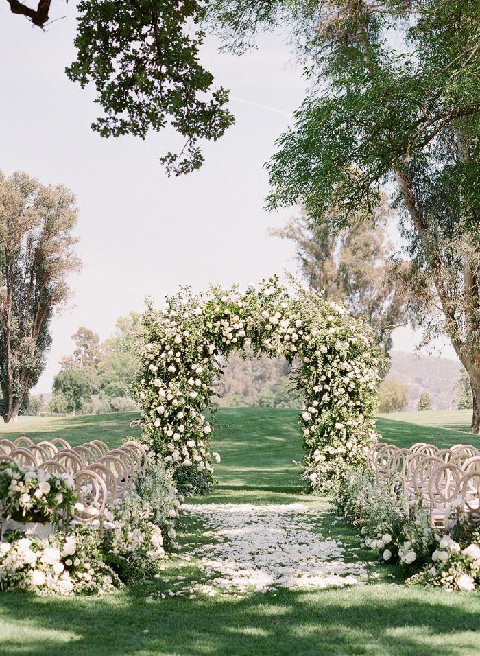 an outdoor wedding ceremony setup with white flowers and greenery on the aisle, surrounded by trees