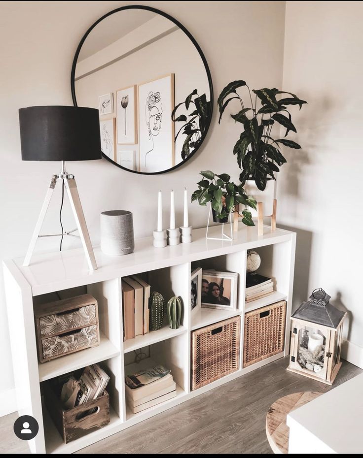 a white shelf with books and plants on it next to a round mirror in the corner