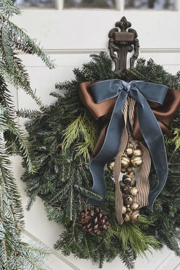 a wreath hanging on the front door with pine cones, bells and blue ribbon tied around it