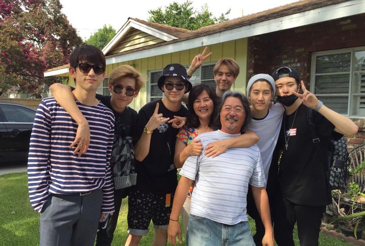 a group of people posing for a photo in front of a house with their arms around each other