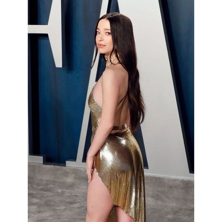 a woman in a gold dress is standing on the red carpet with her back turned