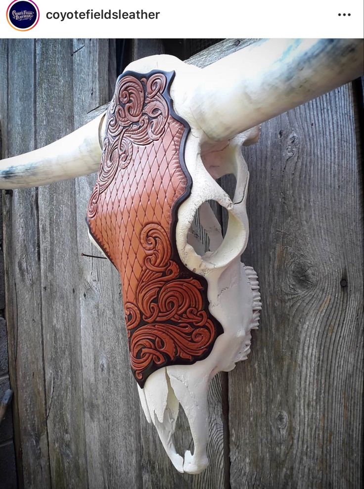 a cow skull with intricate designs on it's side hanging from a wooden fence