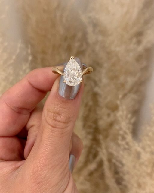 a woman's hand holding an engagement ring with a pear shaped diamond on it