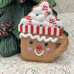 a gingerbread christmas cookie ornament sitting on a table next to a tree