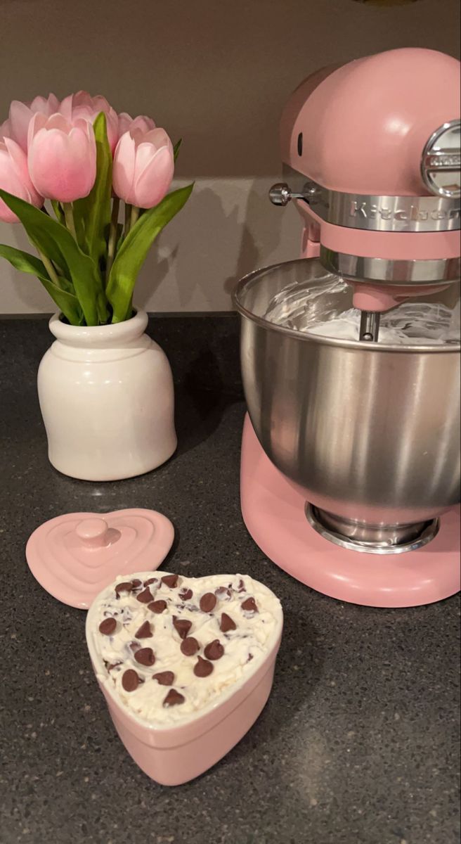 a heart shaped cake sitting on top of a counter next to a mixer and pink tulips