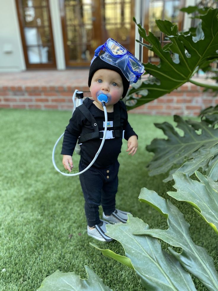 a small boy wearing a hat and holding a hose in his mouth while standing on the grass