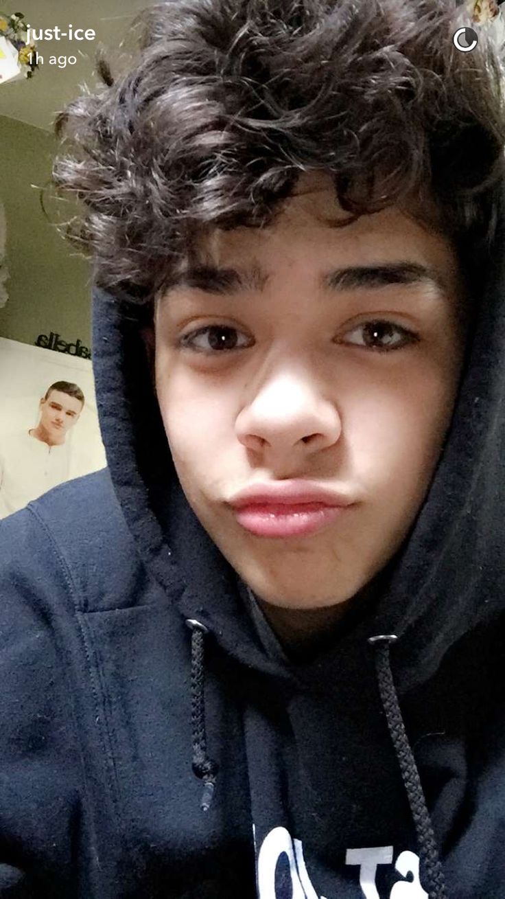 a young boy with curly hair wearing a hoodie and looking at the camera while taking a selfie