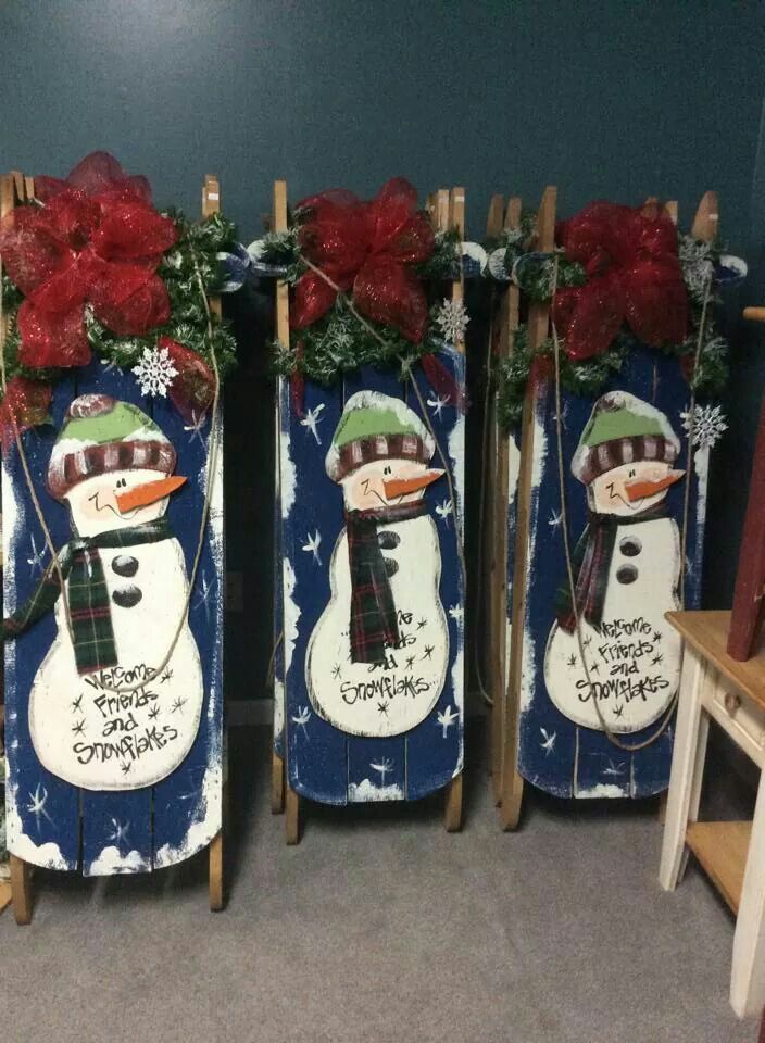 three snowmen decorated with red poinsettis on sled poles in front of a blue wall