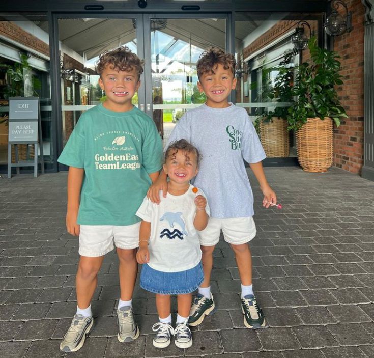 three young boys standing next to each other in front of a building with glass doors