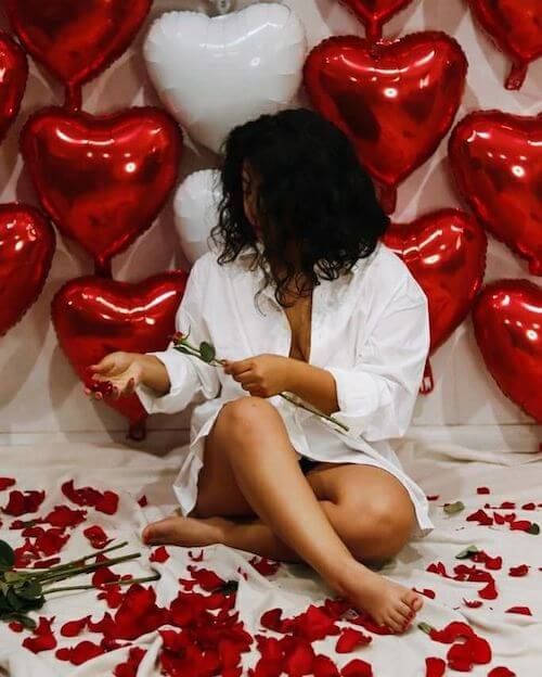 a woman sitting on the floor surrounded by red and white heart shaped balloons with roses