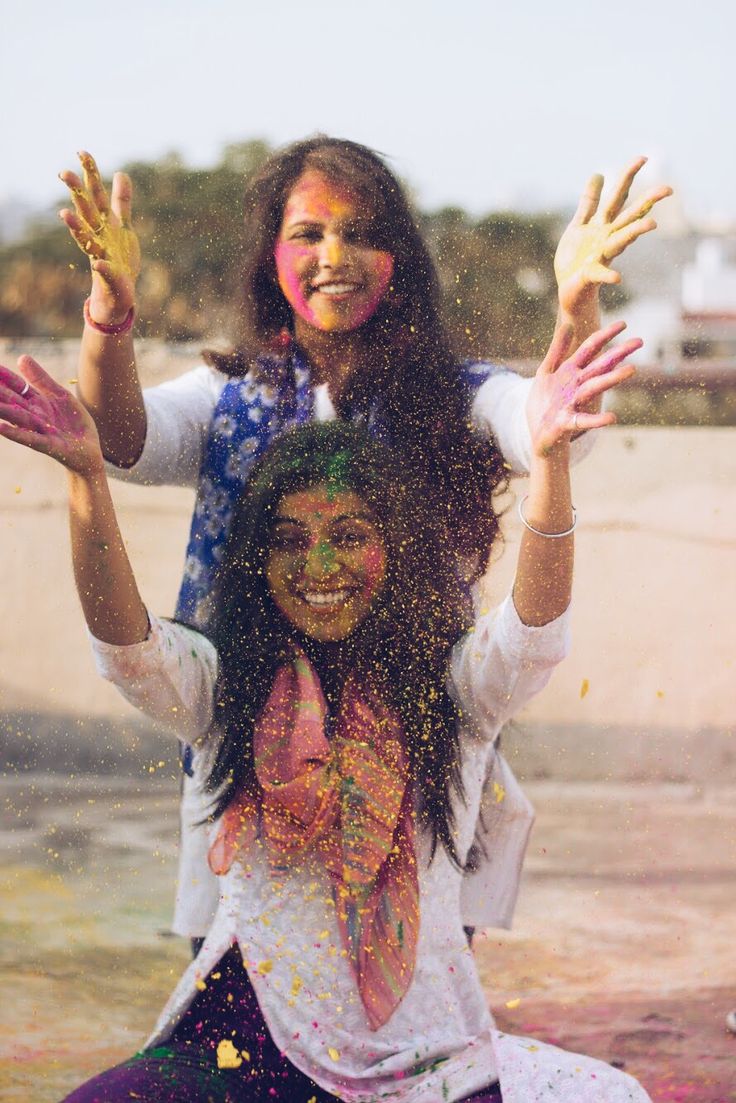 two women covered in colored powder sitting on the ground with their arms spread wide open