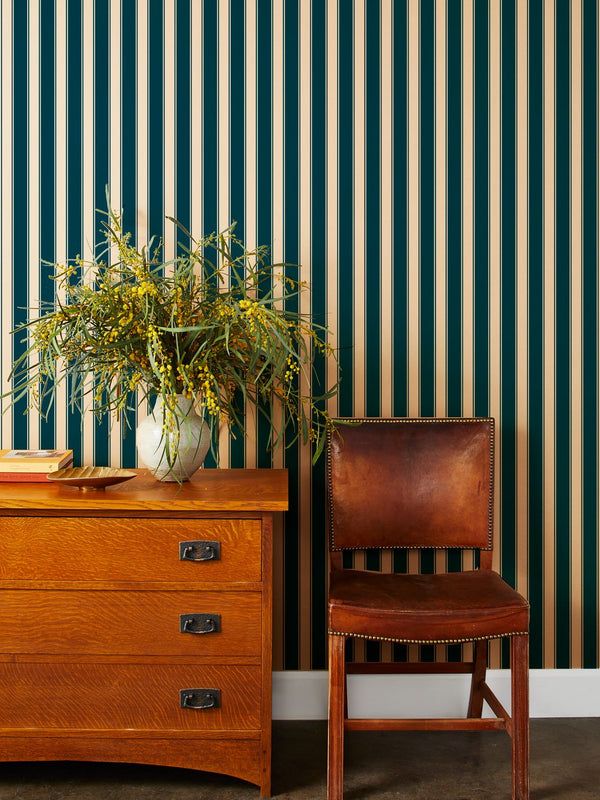 a chair next to a dresser with a potted plant on it and a striped wallpaper behind it