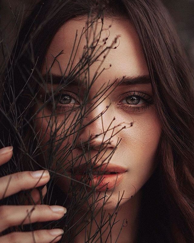 a black and white photo of a woman's face with branches in front of her