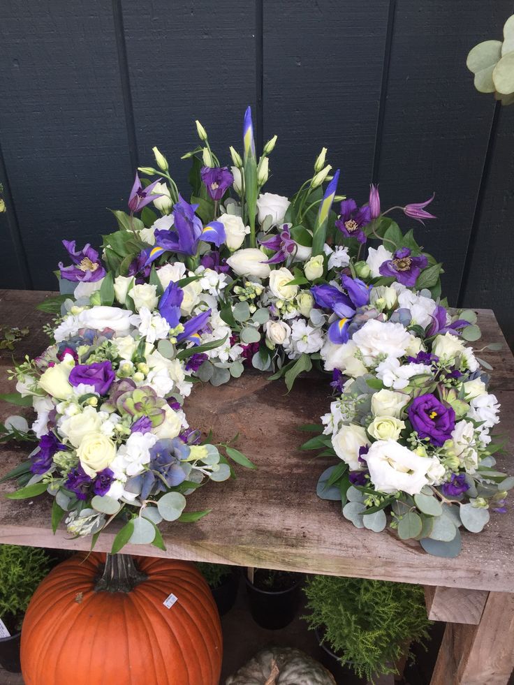 a wreath made out of flowers and greenery sits on a wooden table in front of a black wall