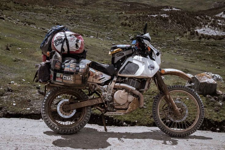 a dirt bike parked on the side of a road next to a grassy field and hill