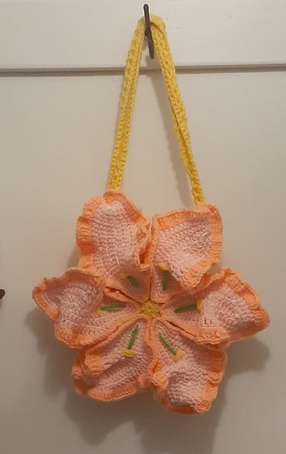 an orange flower hanging from a hook on a white wall next to a yellow string