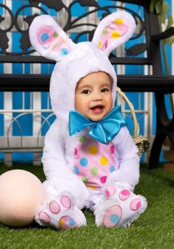 a baby dressed up as a bunny sitting on the grass next to an egg in front of a bench