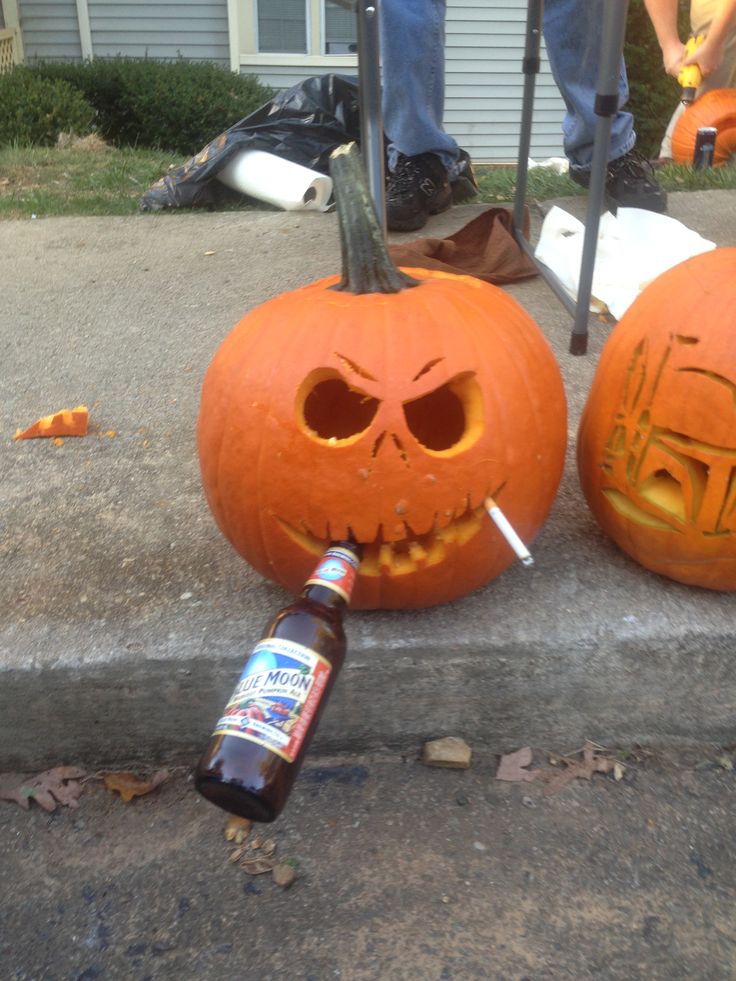 two pumpkins with faces carved into them and one has a beer bottle in its mouth