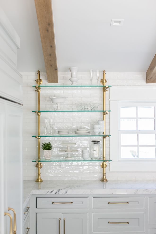 a kitchen with white cabinets and gold pulls on the glass shelving above the sink