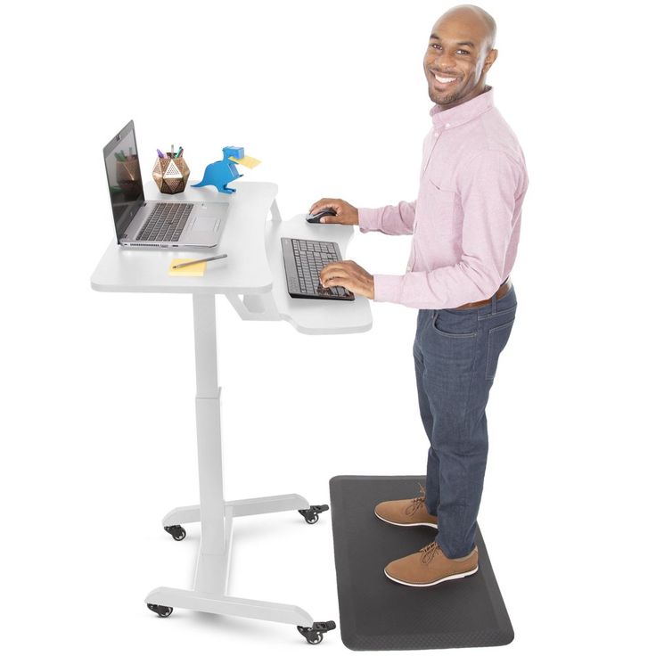 a man standing at a desk using a laptop computer on top of a black mat