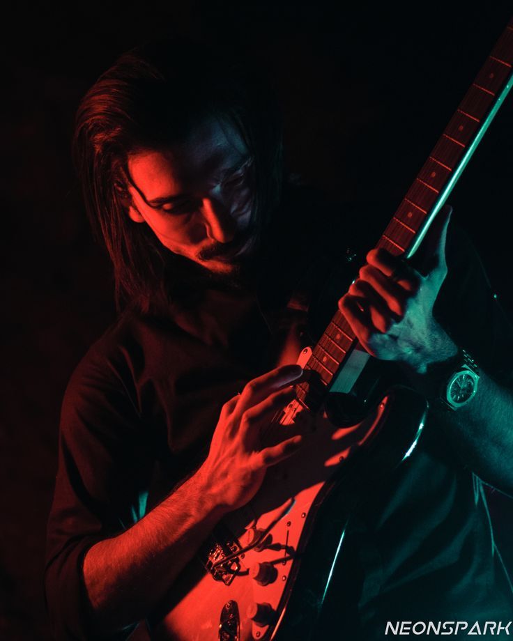 a man with long hair playing an electric guitar in the dark, while wearing a black shirt