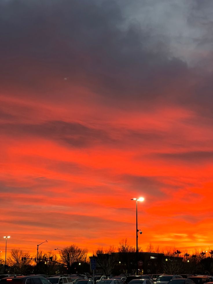 a parking lot filled with lots of parked cars under a red and orange sky at night