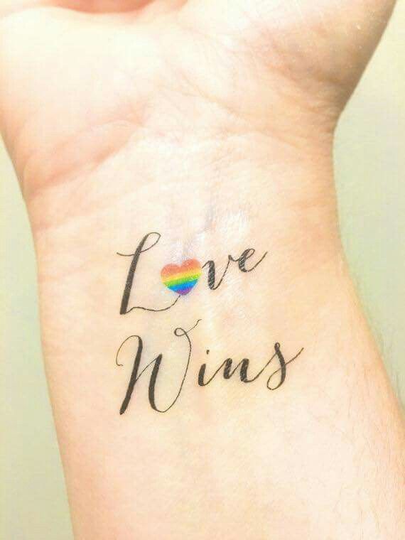 a woman's wrist with the words love wins on it and a rainbow heart