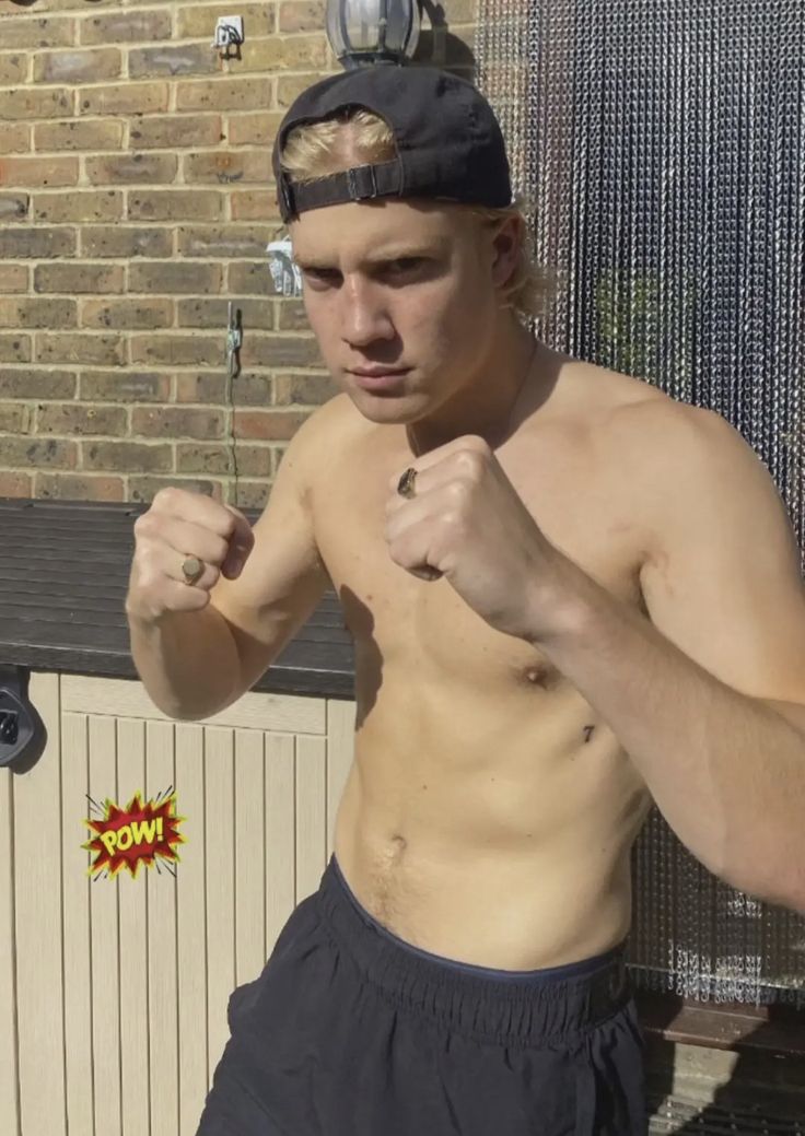 a shirtless man with no shirt on standing in front of a brick wall and holding his fist up