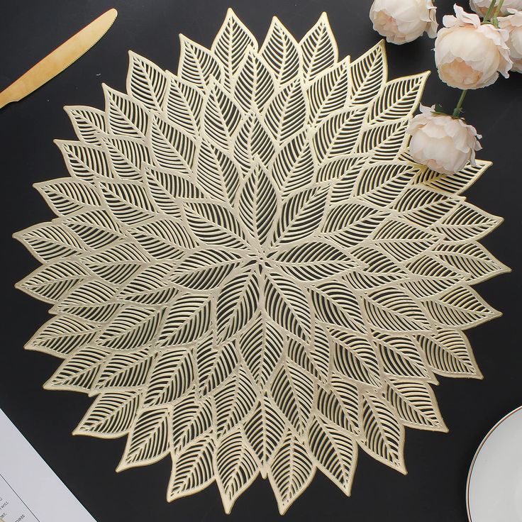 an intricately designed gold paper doily on a black surface with flowers and scissors