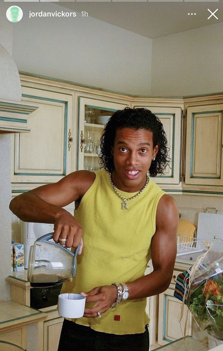 a man in a yellow shirt is pouring something into a white cup and smiling at the camera