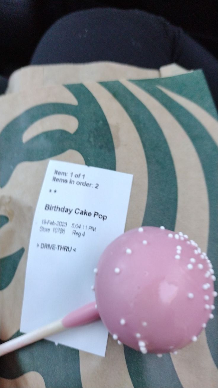 a pink cake pop sitting on top of a table next to a piece of paper