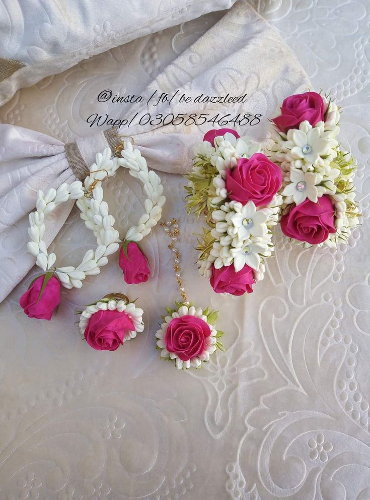 pink and white flowers sitting on top of a bed next to two pairs of earrings