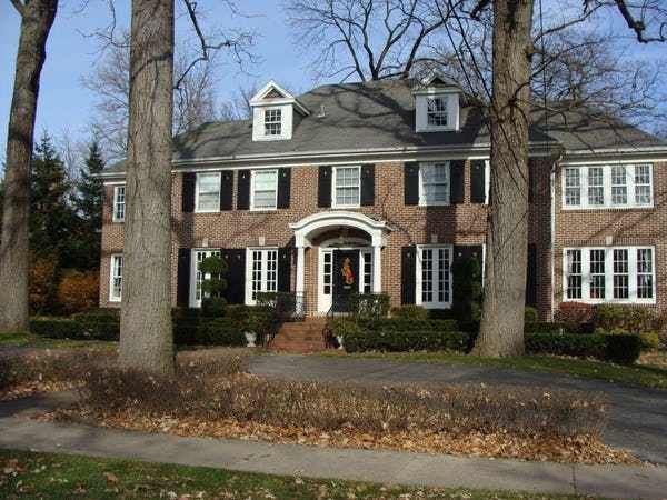 a large brick house with black shutters and white trim on the front door is surrounded by leafy trees