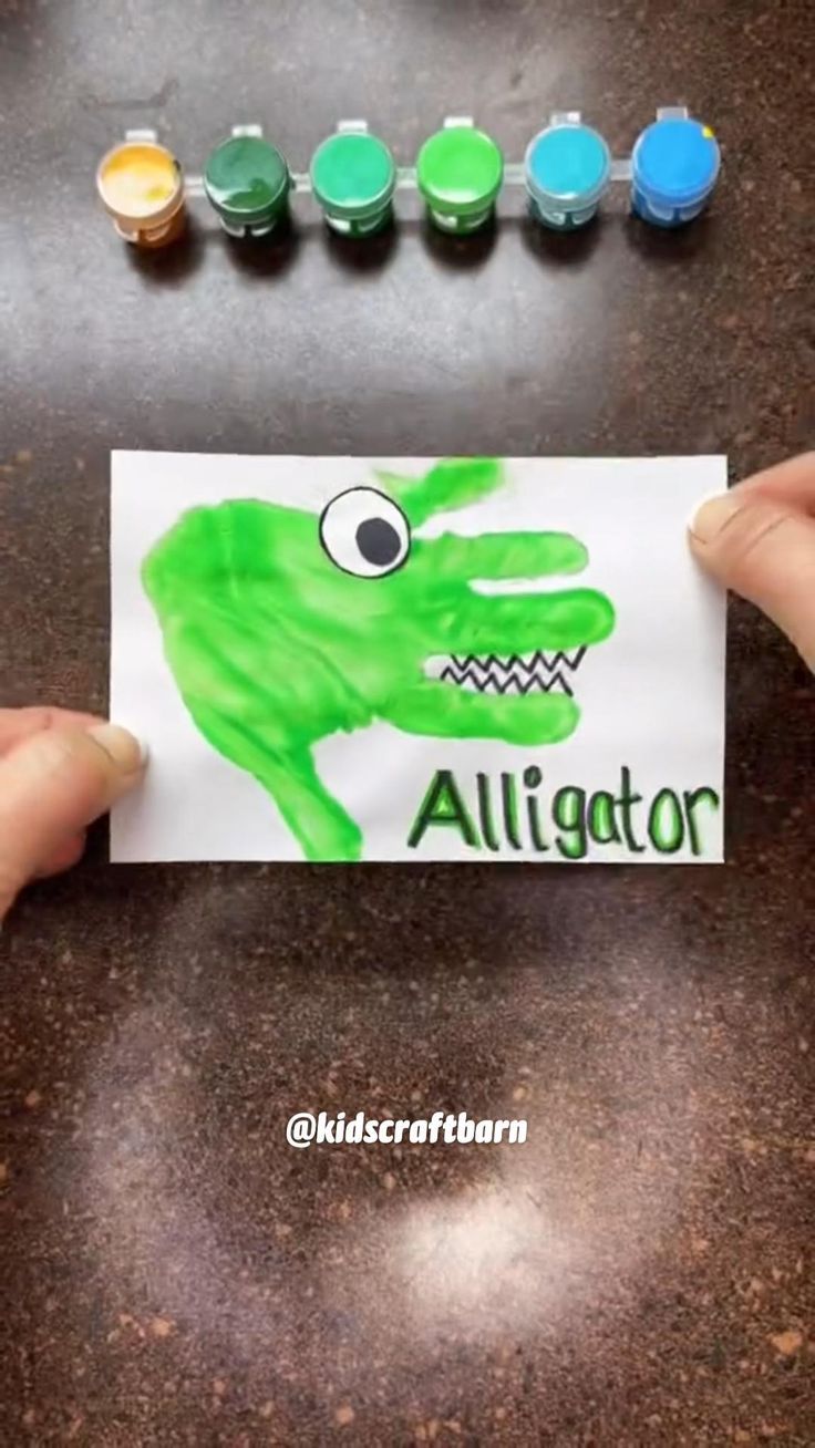 someone is holding up a card with an image of a green alligator on it and some markers