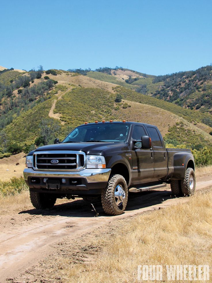 a truck is parked on the side of a dirt road with hills in the background