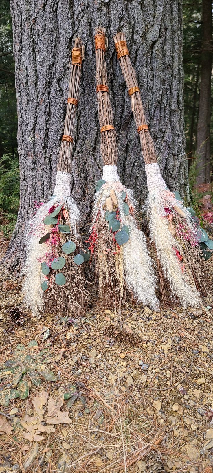 three brooms made out of branches and leaves are hanging from a tree in the woods